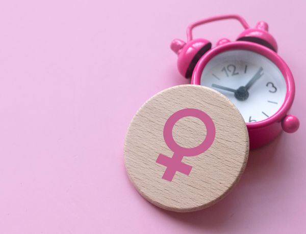 Rosa Symbol auf pinkem Hintergrund und Wecker als Symbol für Wechseljahre.