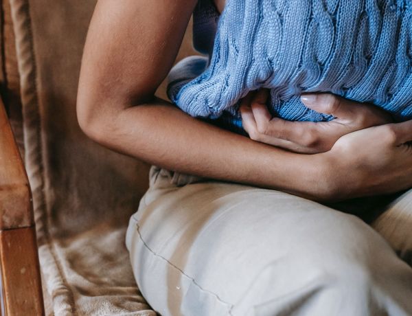 Frau hält sitzend beide Hände auf den Bauch als Zeichen für Verdauung und Bauchschmerzen
