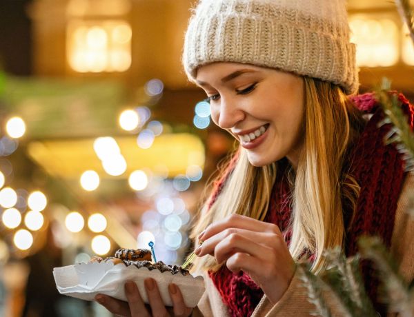 Frau probiert Süßes auf einem festlich dekorierten Weihnachtsmarkt.