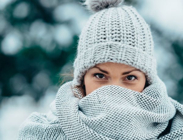 Frau trägt Schal und Mütze im Schnee, Symbol für Hautpflege im Winter.