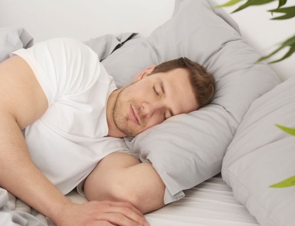 Mann liegt auf der Seite im Bett und schläft mit geschlossenen Augen.