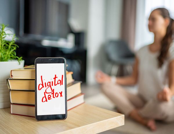 Frau macht Yoga-Übung, davor steht ein Schild mit dem Wort „Digital Detox“.