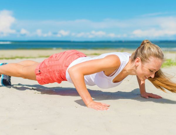 Junge Frau macht Liegestütze am Strand als Symbol für Fitness und Bewegung.