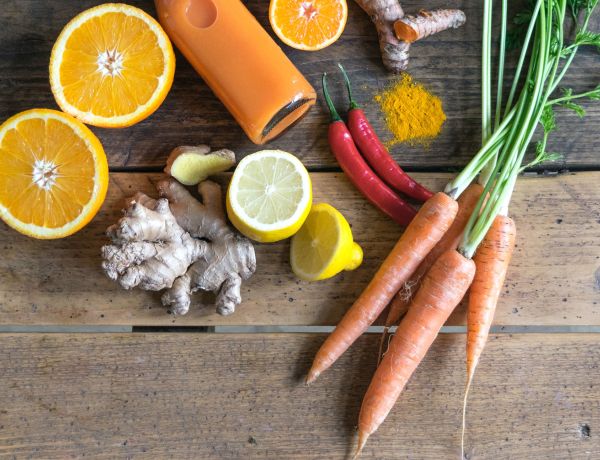 Frisches Obst und Gemüse wie Orangen, Karotten und Ingwer auf einem Holztisch.