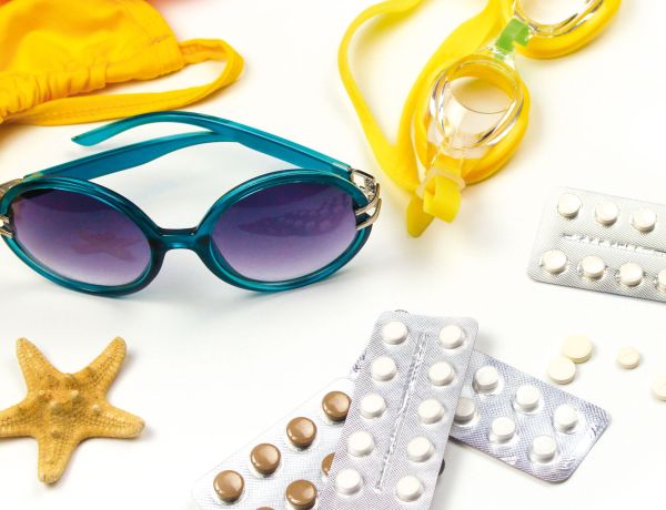 Sonnenbrille, Seestern und Medikamente auf weißen Hintergrund als Darstellung einer Reiseapotheke.