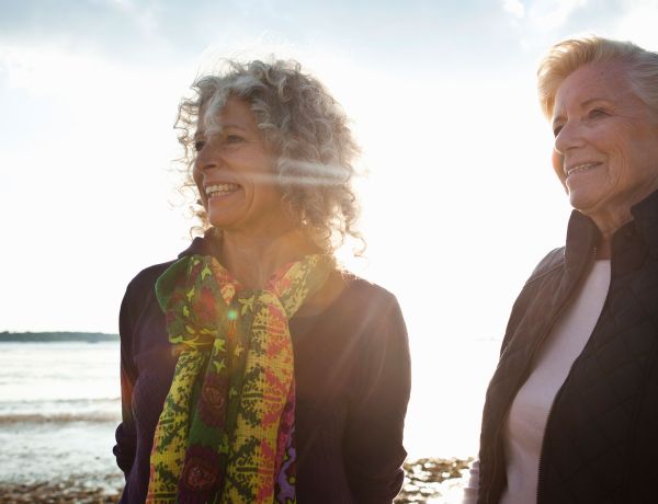 Zwei Frauen mittleren Alters stehen im Freien und lachen freundlich