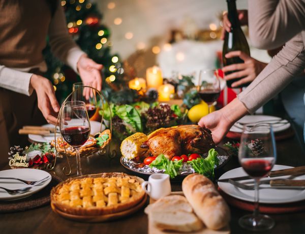 Familie sitzt am gedeckten Tisch mit Braten, Gemüse und Kerzen zur Weihnachtsfeier.