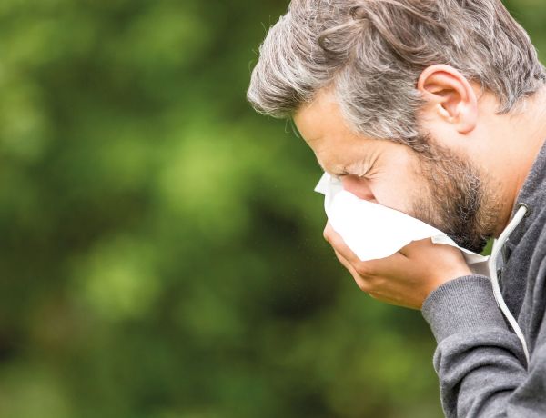 Älterer Mann steht im Grünen und putzt sich die Nase wegen Pollenallergie.