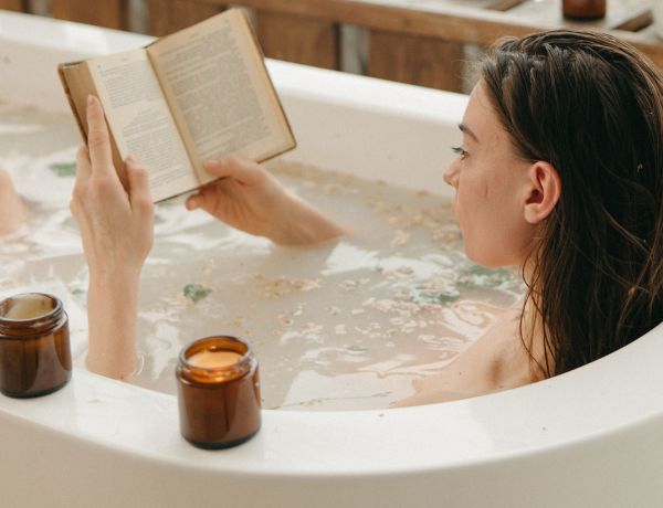 Frau liegt entspannt in einer Badewanne und liest ein Buch