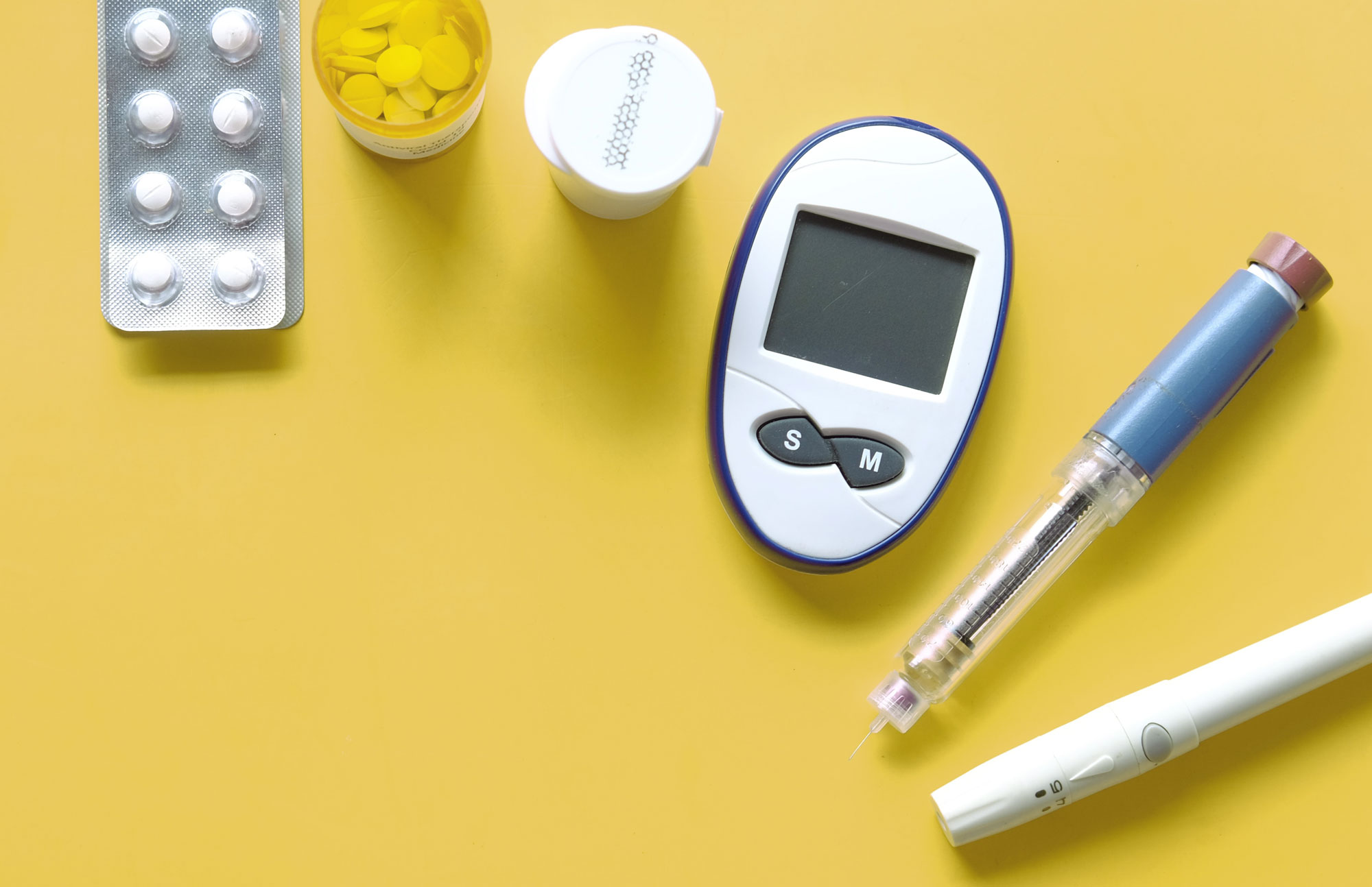 Blutzuckermessgeräte, Teststreifen und Insulinutensilien auf gelbem Hintergrund als Darstellung der Diabetes-Therapie