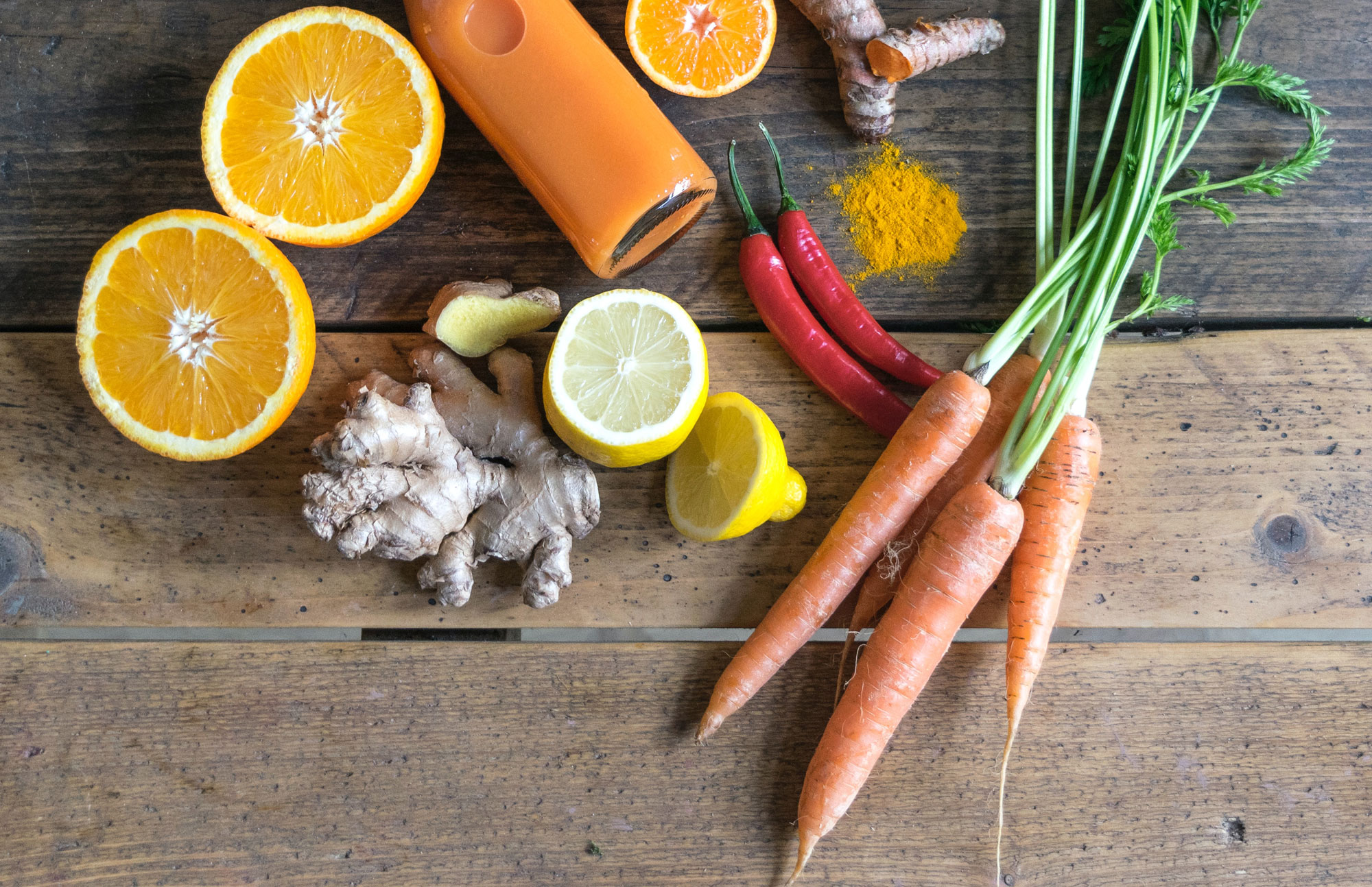Frisches Obst und Gemüse wie Orangen, Karotten und Ingwer auf einem Holztisch.