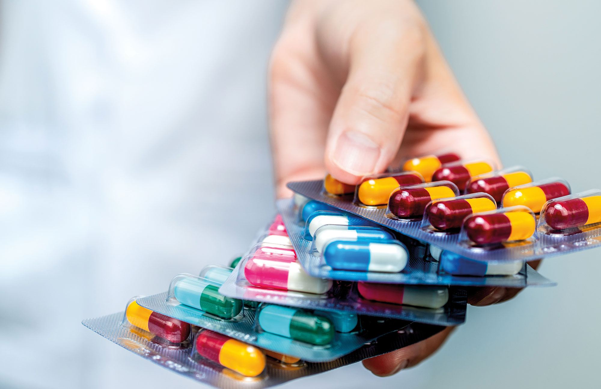 Hand hält verschiedene Tabletten und Blisterpackungen als Symbol für Arzneimittel.