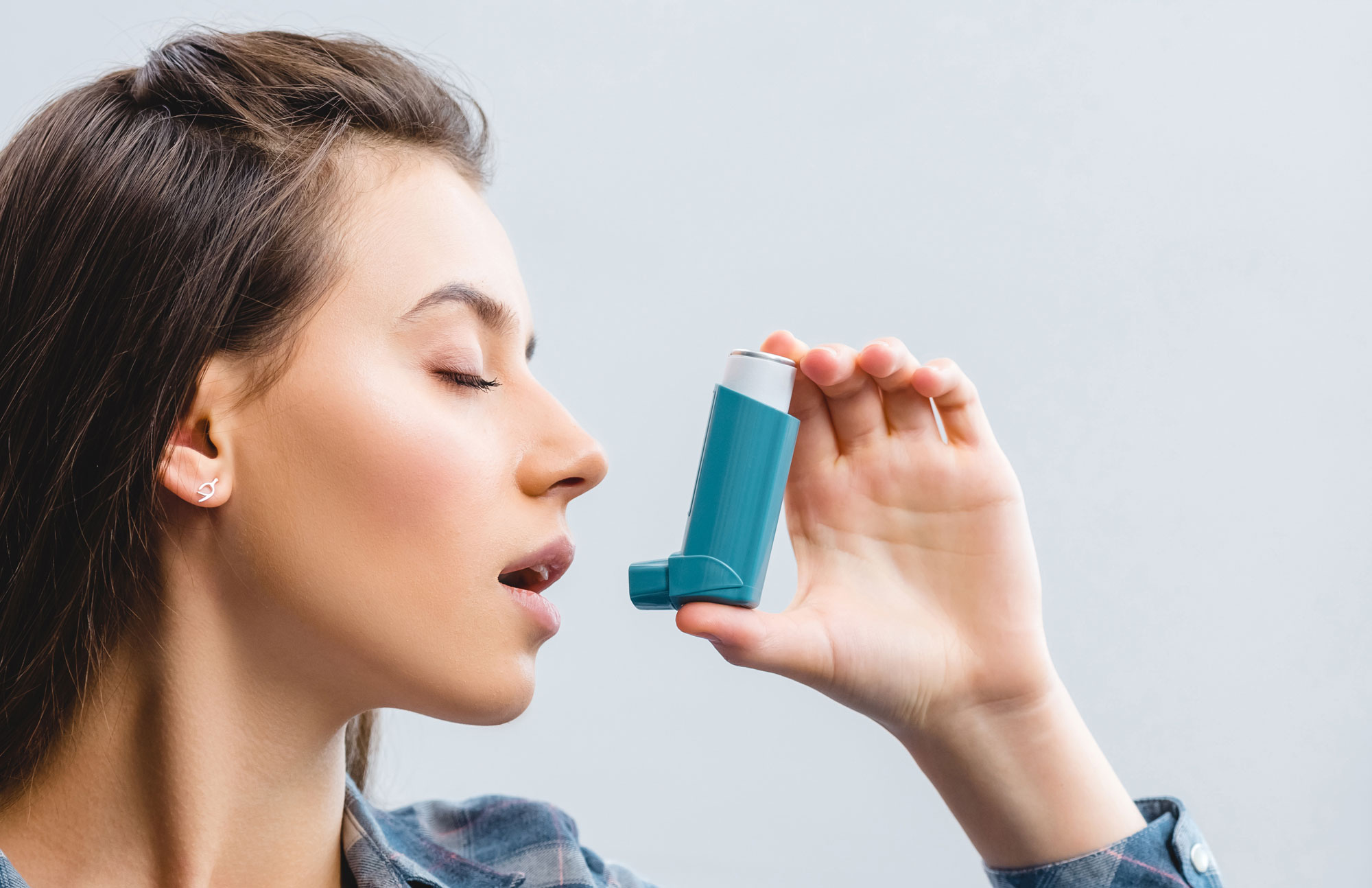 Junge Frau benutzt einen Asthma-Inhalator gegen Atembeschwerden.