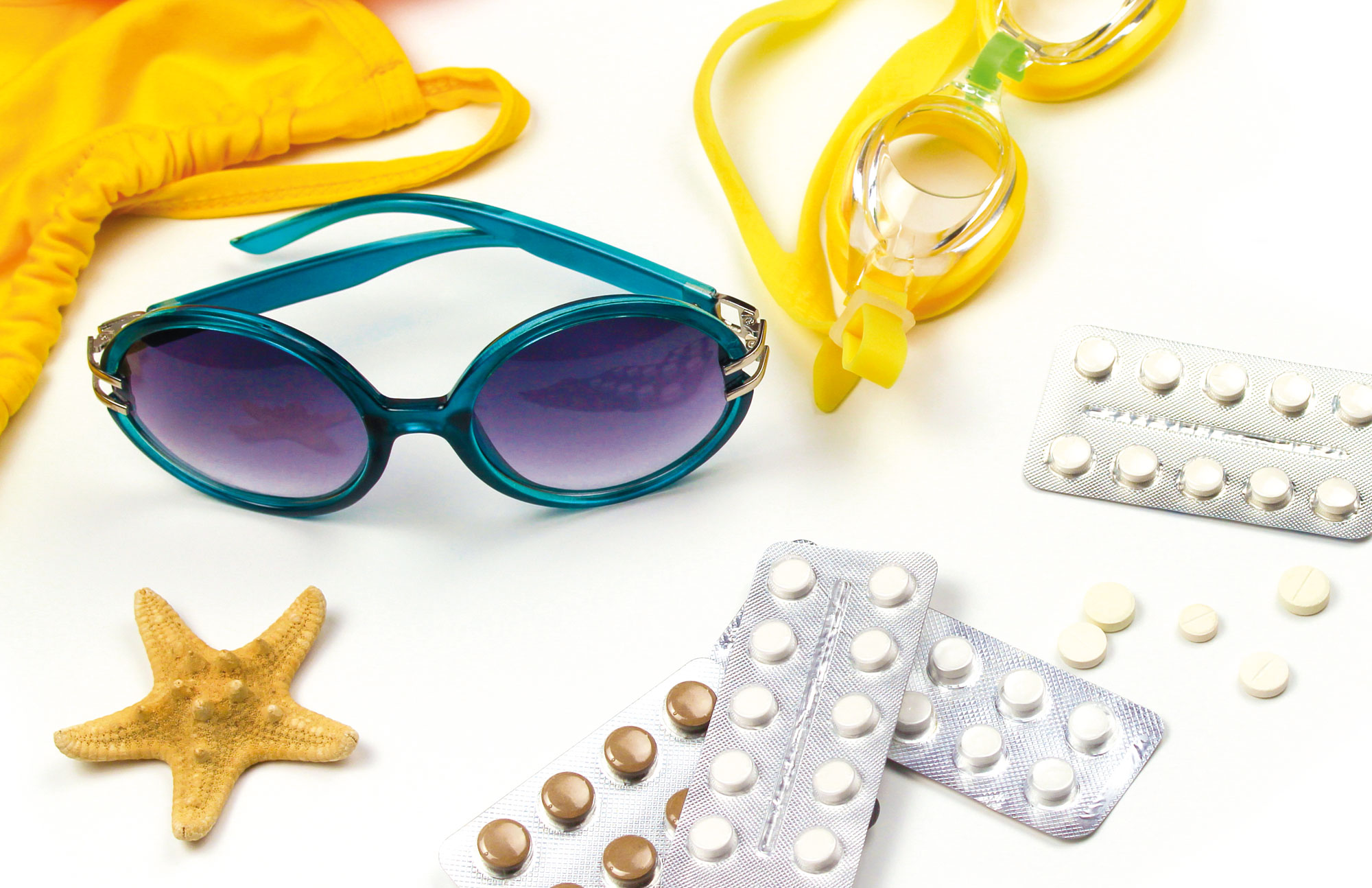Sonnenbrille, Seestern und Medikamente auf weißen Hintergrund als Darstellung einer Reiseapotheke.