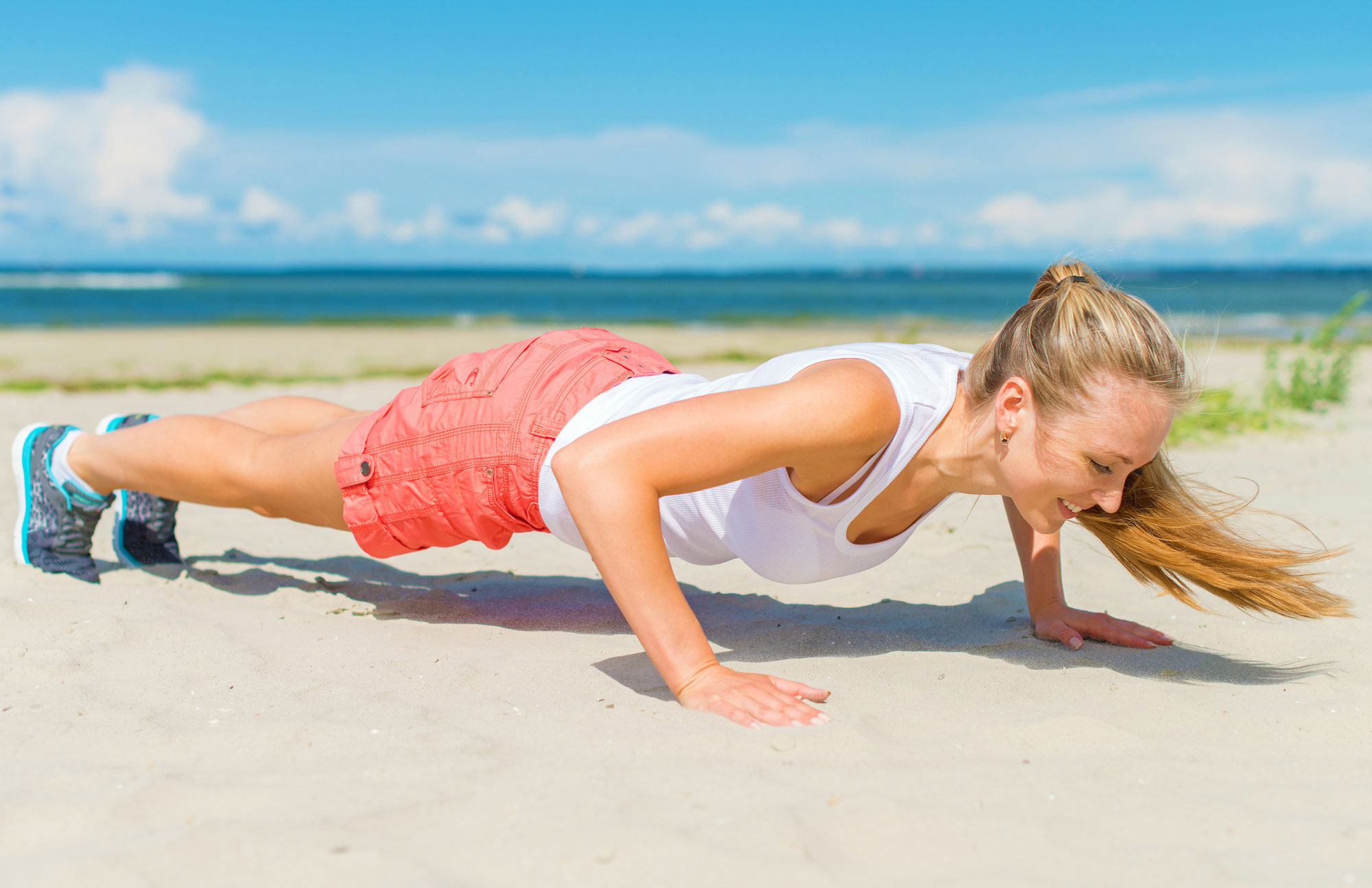 Junge Frau macht Liegestütze am Strand als Symbol für Fitness und Bewegung.