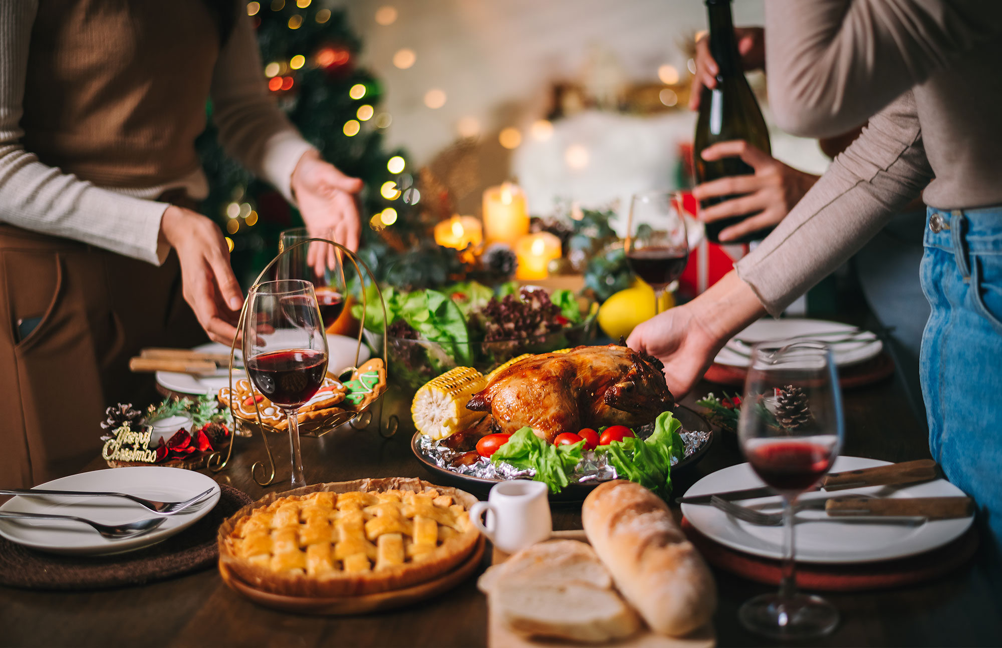 Familie sitzt am gedeckten Tisch mit Braten, Gemüse und Kerzen zur Weihnachtsfeier.