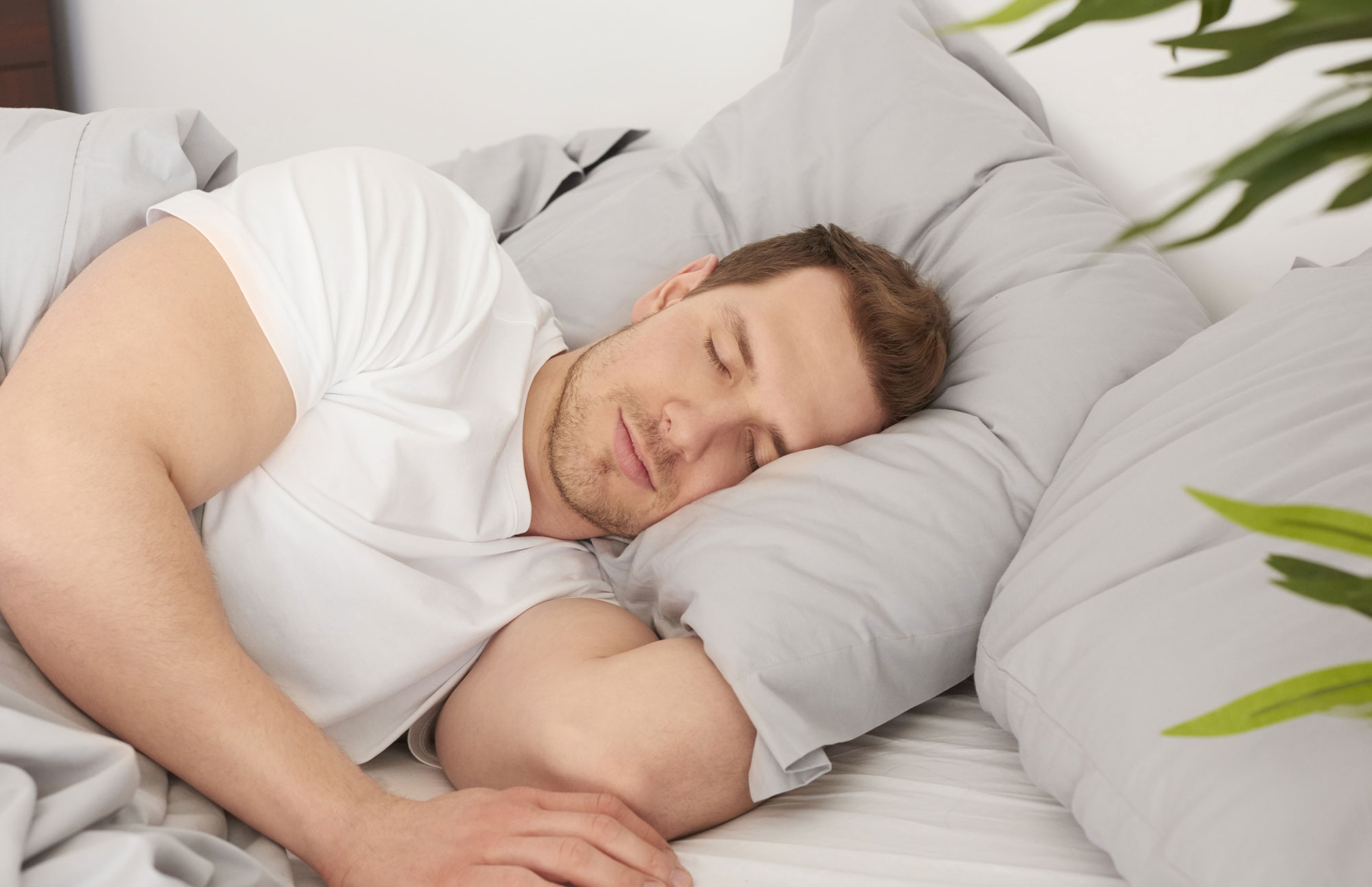 Mann liegt auf der Seite im Bett und schläft mit geschlossenen Augen.