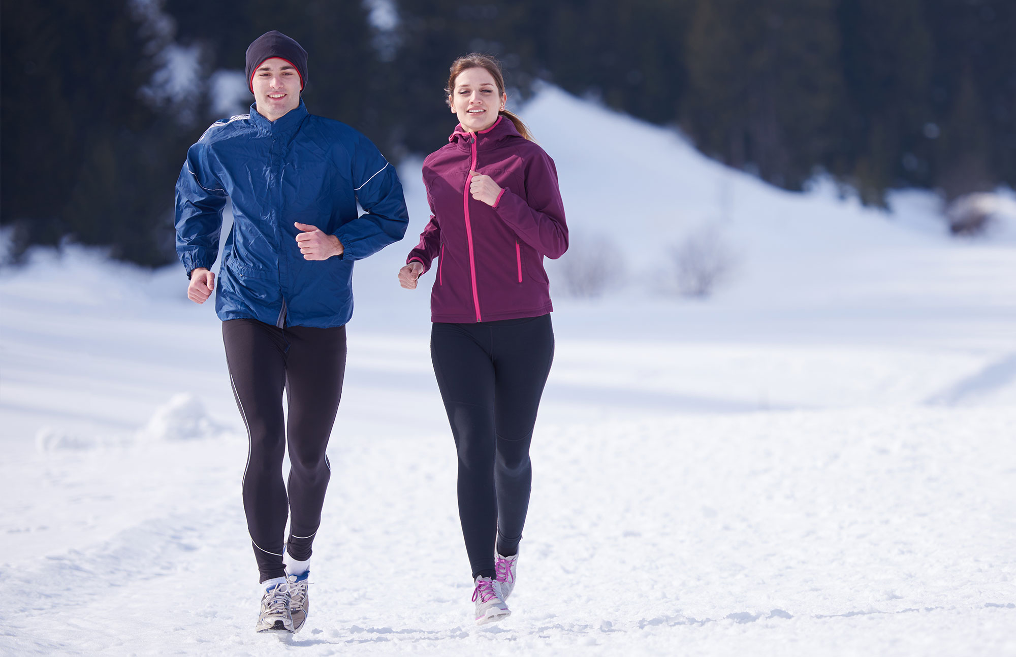 Zwei Personen laufen in Sportkleidung auf verschneitem Weg in winterlicher Landschaft.
